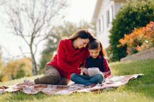 A woman and child sit on a blanket in a sunny backyard