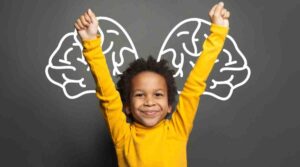 A child in a bright yellow sweater raises both arms triumphantly