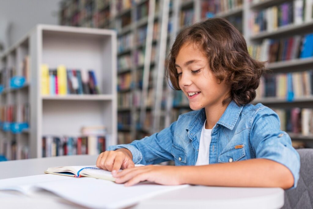 A young person in a denim jacket sits at a table, focused on an open book