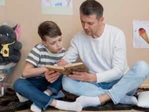 A parent and child sit together on a blanket, reading a book