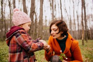 A child in a colorful plaid coat hands a small white flower to a woman