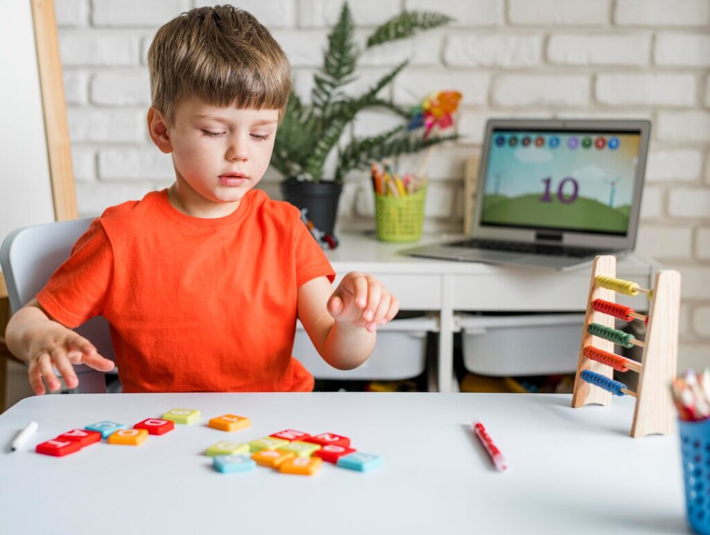 A child in an orange shirt sits at a table, engaging with colorful number tiles