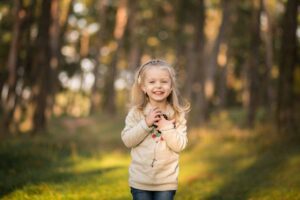 A child stands in a sunlit forest, holding a small camera