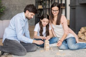 A family plays with a wooden block game in a cozy living room.