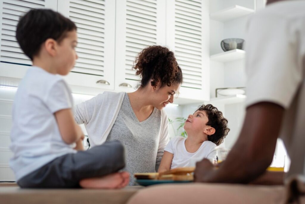 A mother and her two sons enjoying a conversation in a bright kitchen.