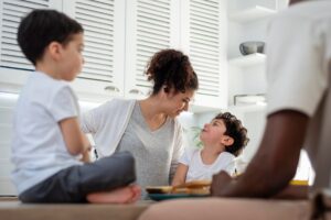 A mother and her two sons enjoying a conversation in a bright kitchen.