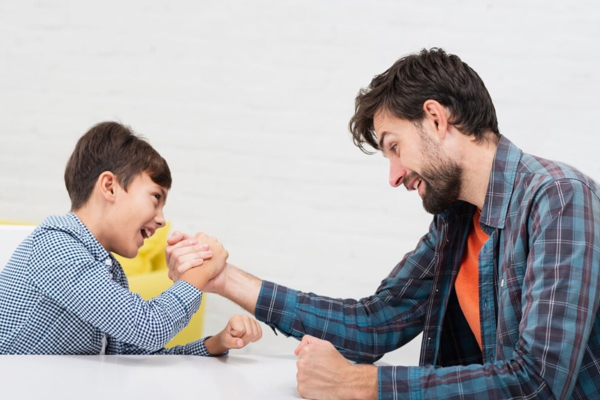 A man and a boy happily engaging in an arm-wrestling contest at a table.