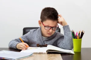 A child sits at a table, thinking with one hand on their forehead